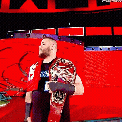 A Wrestler Is Holding A World Heavyweight Championship Belt While Standing On A Red Stage . GIF