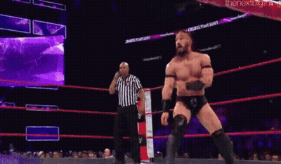 A Wrestler Is Jumping In The Air While Another Wrestler Is Standing Next To Him In A Wrestling Ring . GIF