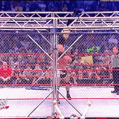 A Wrestler Is Jumping Over A Chain Link Fence While A Referee Looks On GIF