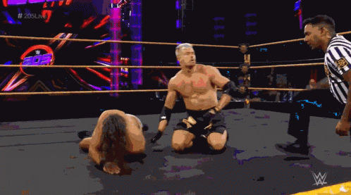 A Wrestler Is Kneeling Down In A Wrestling Ring While A Referee Watches GIF