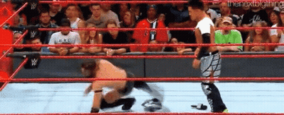 A Wrestler Is Kneeling Down In A Wrestling Ring While Another Wrestler Looks On . GIF