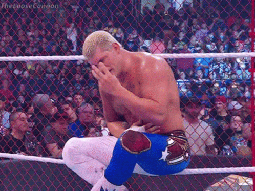 A Wrestler Is Kneeling Down In A Wrestling Ring With His Hand On His Face . GIF