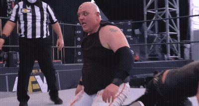 A Wrestler Is Kneeling Down In Front Of A Referee Wearing A Shirt That Says Aew GIF