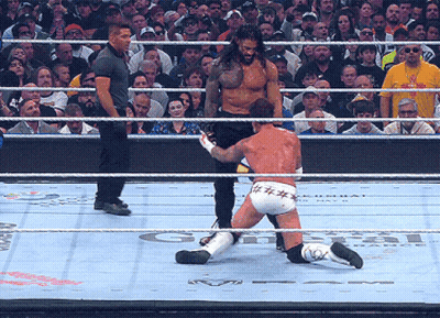 A Wrestler Is Kneeling Down In The Ring While A Referee Looks On GIF