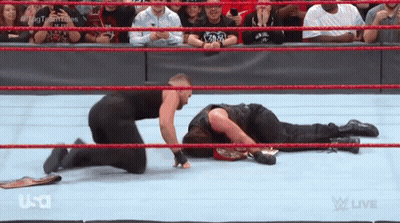 A Wrestler Is Kneeling Down Next To Another Wrestler Who Is Laying On The Floor . GIF