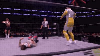 A Wrestler Is Laying On The Ground In A Wrestling Ring While A Referee Watches GIF