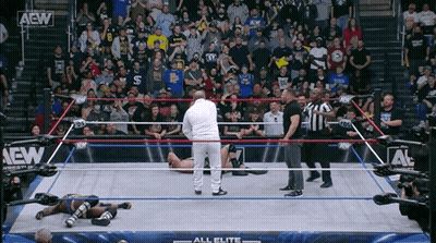 A Wrestler Is Laying On The Ground In A Wrestling Ring With A Crowd Watching GIF