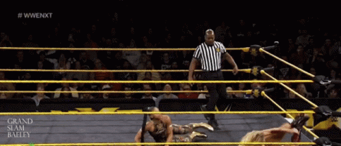 A Wrestler Is Laying On The Ground In A Wrestling Ring With A Referee In The Background GIF