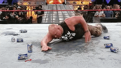 A Wrestler Is Laying On The Ground In A Wrestling Ring With Beer Cans . GIF