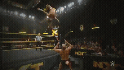 A Wrestler Is Laying On The Ground In Front Of A Sign That Says Nxt On It GIF