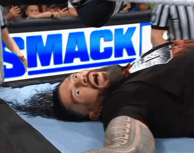 A Wrestler Is Laying On The Ground In Front Of A Smack Sign GIF