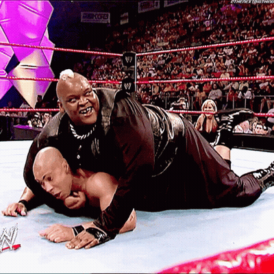 A Wrestler Is Laying On The Ground While Another Wrestler Holds Onto Him GIF