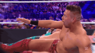 A Wrestler Is Laying On The Ground With His Arm Outstretched In A Wrestling Ring . GIF