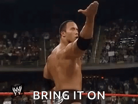 A Wrestler Is Raising His Fist In The Air In Front Of A Crowd And Says `` Bring It On '' . GIF