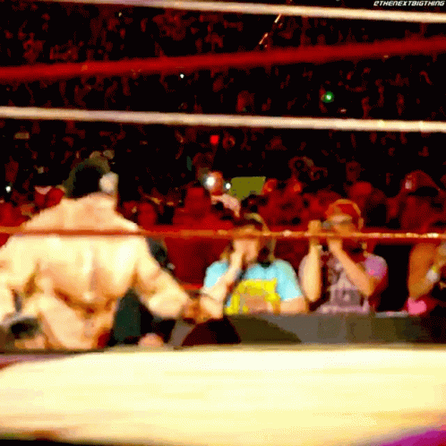 A Wrestler Is Shaking Hands With Another Wrestler In A Wrestling Ring While A Crowd Watches . GIF