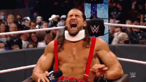 A Wrestler Is Sitting In A Chair With His Mouth Open And A Microphone In His Hand . GIF