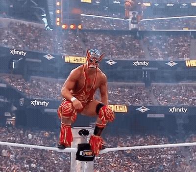A Wrestler Is Sitting On A Rope In Front Of A Crowd With Xfinity Advertisements In The Background GIF