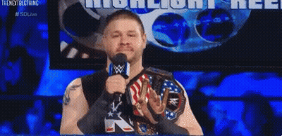 A Wrestler Is Speaking Into A Microphone While Wearing A Wwe Championship Belt . GIF