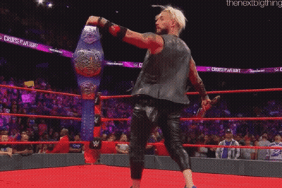 A Wrestler Is Standing In A Ring Holding A Wrestling Championship Belt GIF