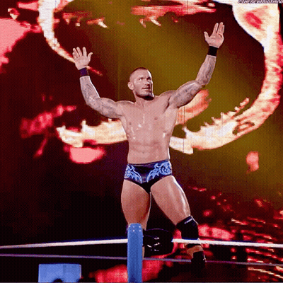 A Wrestler Is Standing In A Ring With His Arms In The Air And A Screen Behind Him That Says Wrestling GIF