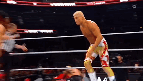 A Wrestler Is Standing In A Wrestling Ring With A Referee In The Background . GIF