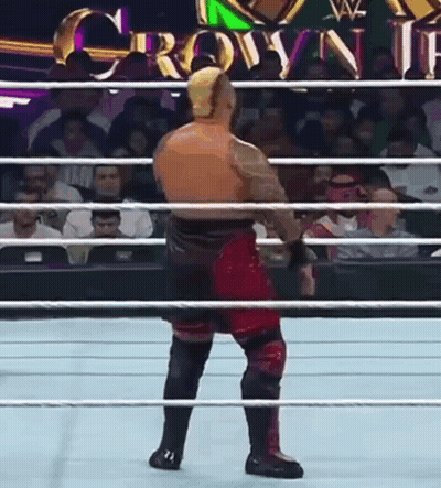A Wrestler Is Standing In The Middle Of A Wrestling Ring With A Crowd Watching . GIF