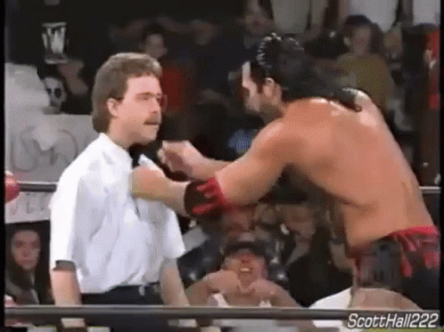 A Wrestler Is Standing Next To A Referee In A Ring While Another Wrestler Is Standing Next To Him . GIF