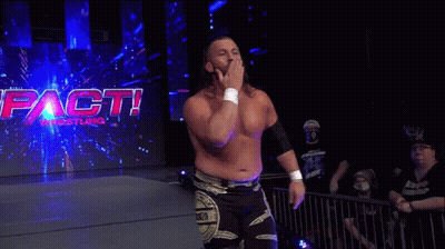 A Wrestler Is Walking In Front Of A Sign That Says Impact Wrestling . GIF
