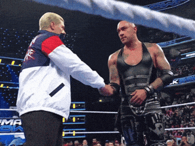 A Wrestler Shakes Hands With A Referee In A Ring That Has The Word Emma On It GIF