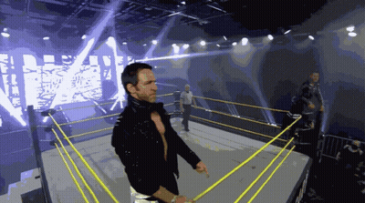A Wrestler Stands In A Wrestling Ring With A Large Screen Behind Him That Says Wrestling GIF