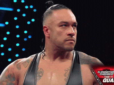 A Wrestler Stands In Front Of A Sign That Says The Elimination Chamber GIF