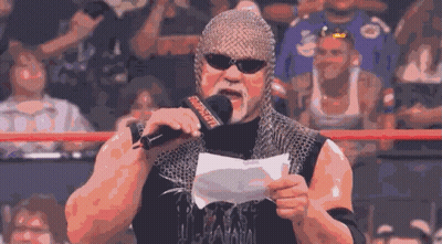 A Wrestler Wearing A Chain Mail Helmet Holds A Piece Of Paper In Front Of A Microphone That Says Wwe GIF