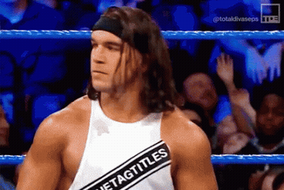 A Wrestler Wearing A Headband And A White Tank Top With A Black Stripe That Says Tag Titles GIF