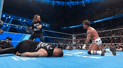 A Wrestler Wearing A Shirt That Says Justice And Sanity Is Standing Next To Another Wrestler GIF