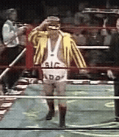 A Wrestler Wearing A Yellow And White Striped Jacket And Shorts With The Word Add On Them Walks Through A Ring GIF
