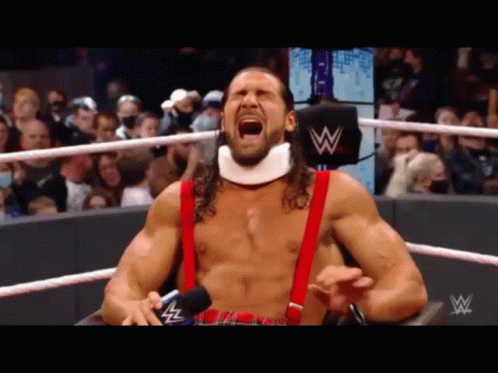 A Wrestler With A Neck Brace And Suspenders Is Screaming In A Ring . GIF