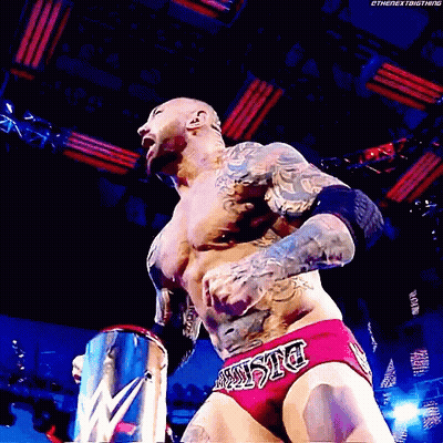 A Wrestler With A Tattoo On His Chest Is Wearing A Pair Of Red Trunks With The Word Justice On The Side GIF