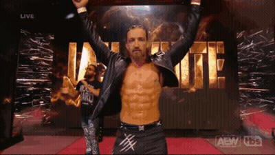 A Wrestler With His Arms In The Air In Front Of A Sign That Says Aew GIF