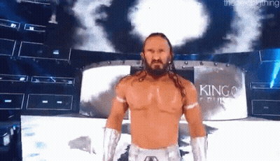 A Wrestler With Long Hair And A Beard Is Standing On A Stage In Front Of A Large Screen . GIF