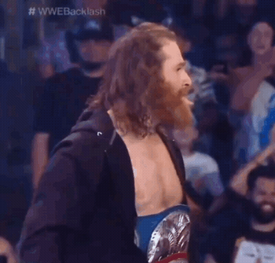 A Wrestler With Long Hair And A Beard Is Wearing A Wrestling Belt . GIF