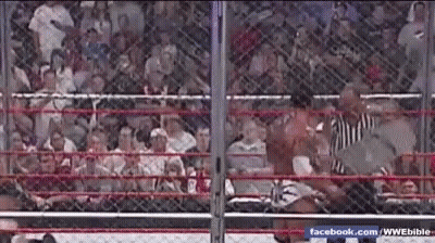 A Wrestling Match Is Being Held In A Cage With A Crowd Watching . GIF