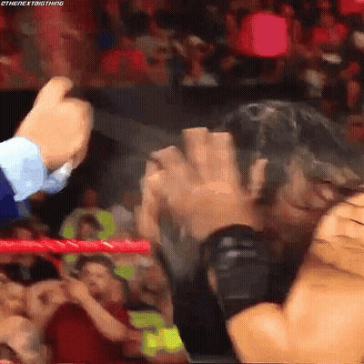 A Wrestling Match Is Going On In A Crowded Stadium And A Man Is Holding Another Man 'S Hand . GIF