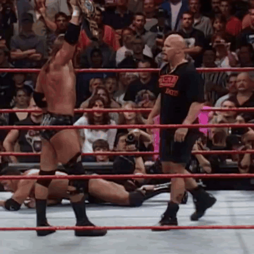 A Wrestling Ring With A Referee And A Wrestler Wearing A T-Shirt That Says World Heavyweight Champion GIF