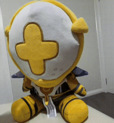 A Yellow And White Stuffed Animal With A Yellow Cross On Its Head Is Sitting On A Bed . GIF