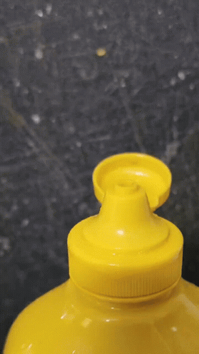 A Yellow Bottle Of Mustard Is Being Poured Into A Yellow Container GIF