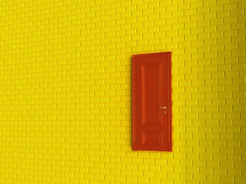 A Yellow Brick Wall With A Red Door That Is Open GIF