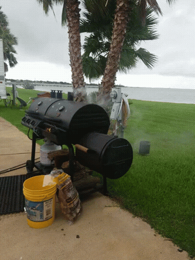 A Yellow Bucket With The Word Fire On It Sits On A Sidewalk Next To A Grill GIF