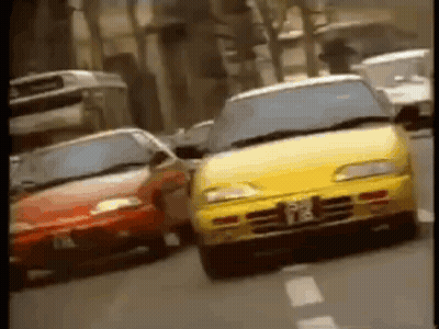A Yellow Car And A Red Car Are Driving Down A City Street . GIF
