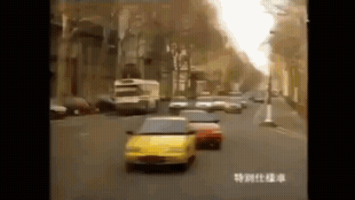 A Yellow Car Is Driving Down A Busy City Street . GIF
