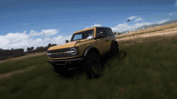 A Yellow Ford Bronco Is Driving Down A Grassy Hill GIF